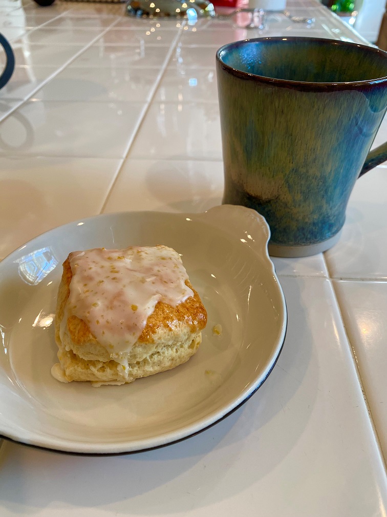Square shaped scone topped with a Citrus, Grand-Marnier Glaze and served next to a cup of tea.