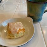 A square shaped scone, topped with a Grand Marnier Citrus Glaze along with a cup of tea